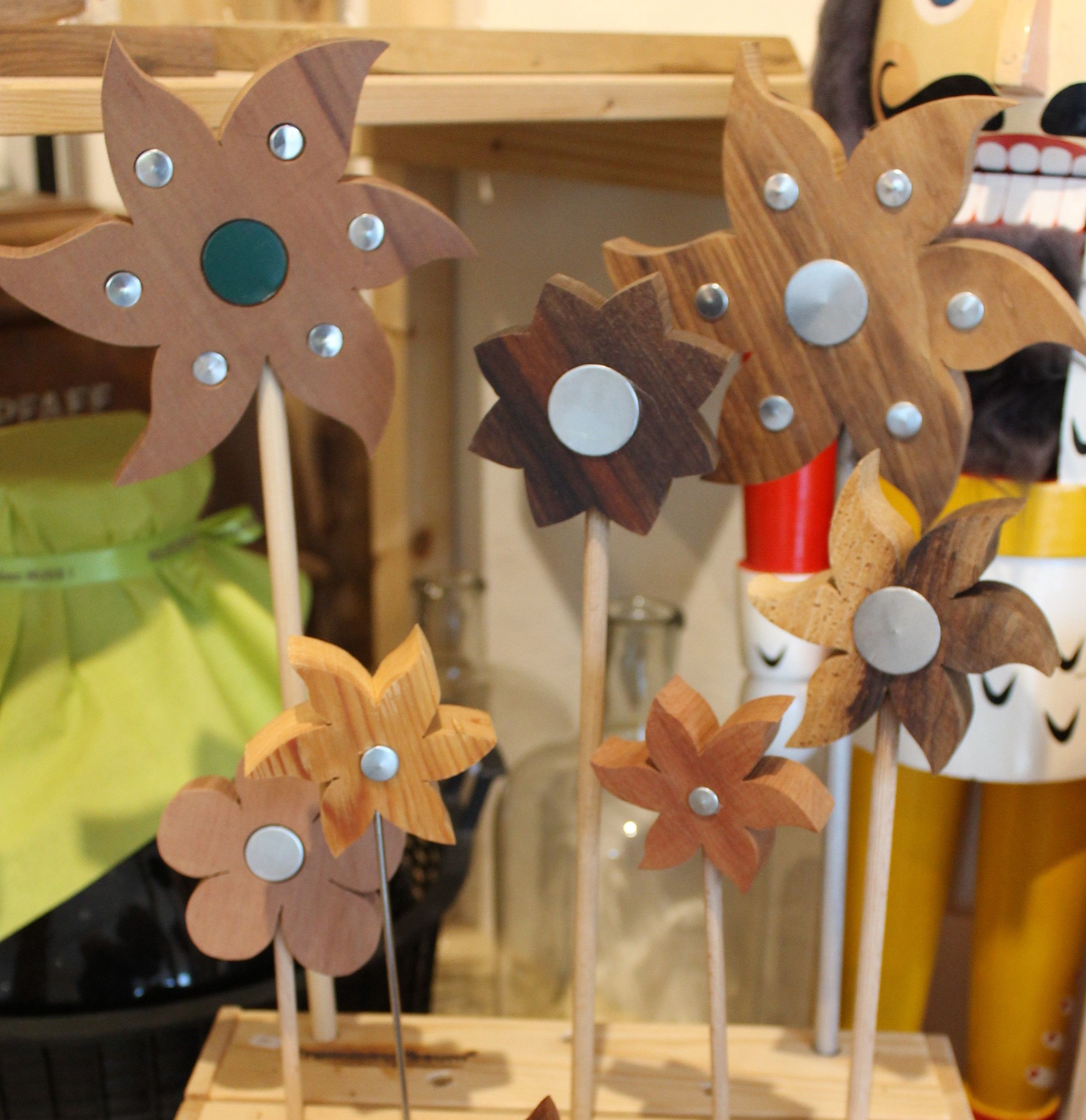 Dřevěné květiny s kovovými ozdobami na tyčích na polici.