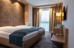 Moderní hotelový pokoj s manželskou postelí, dřevěným obložením a okny se závěsy.