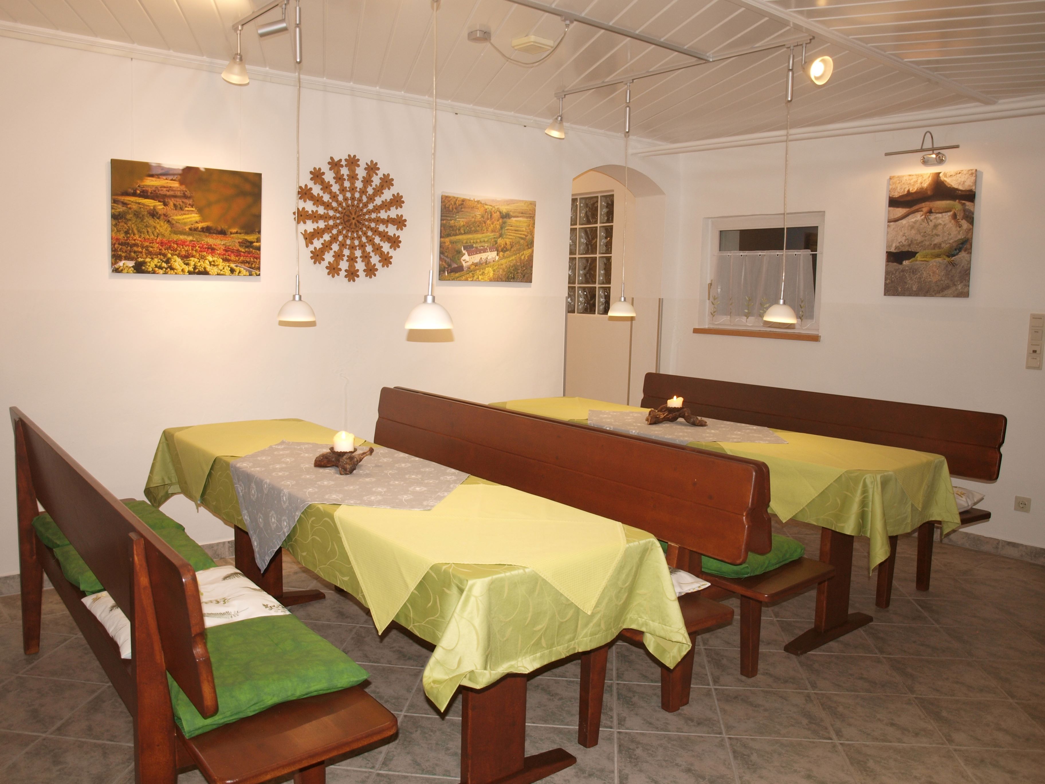 Útulná snídaňová místnost s dřevěnými lavicemi, zelenými ubrusy a nástěnnými dekoracemi.