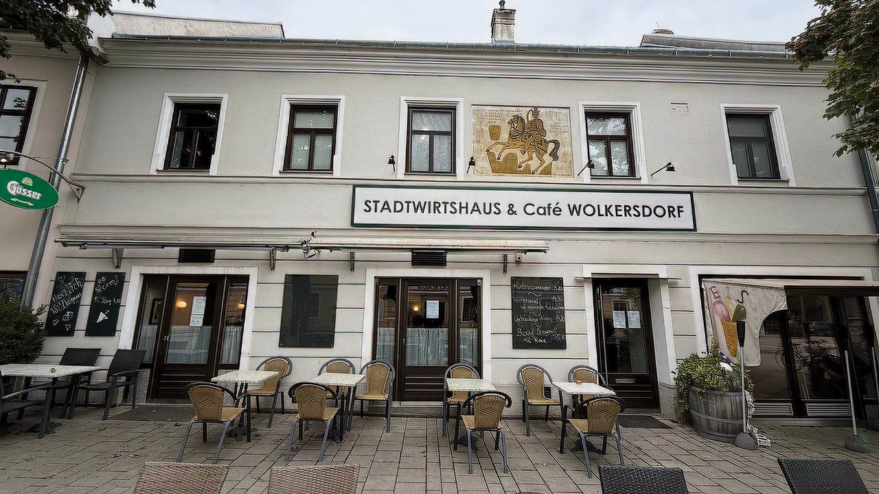 Pohled zvenčí na Stadtwirtshaus & Café Wolkersdorf se stoly a židlemi na terase.