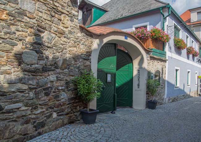 Historická budova se zelenou bránou a květinami.