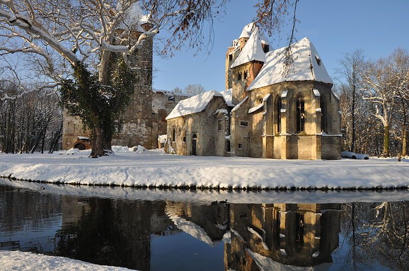 Zřícenina hradu Pottendorf v zimě se sněhem a odrazem ve vodě.