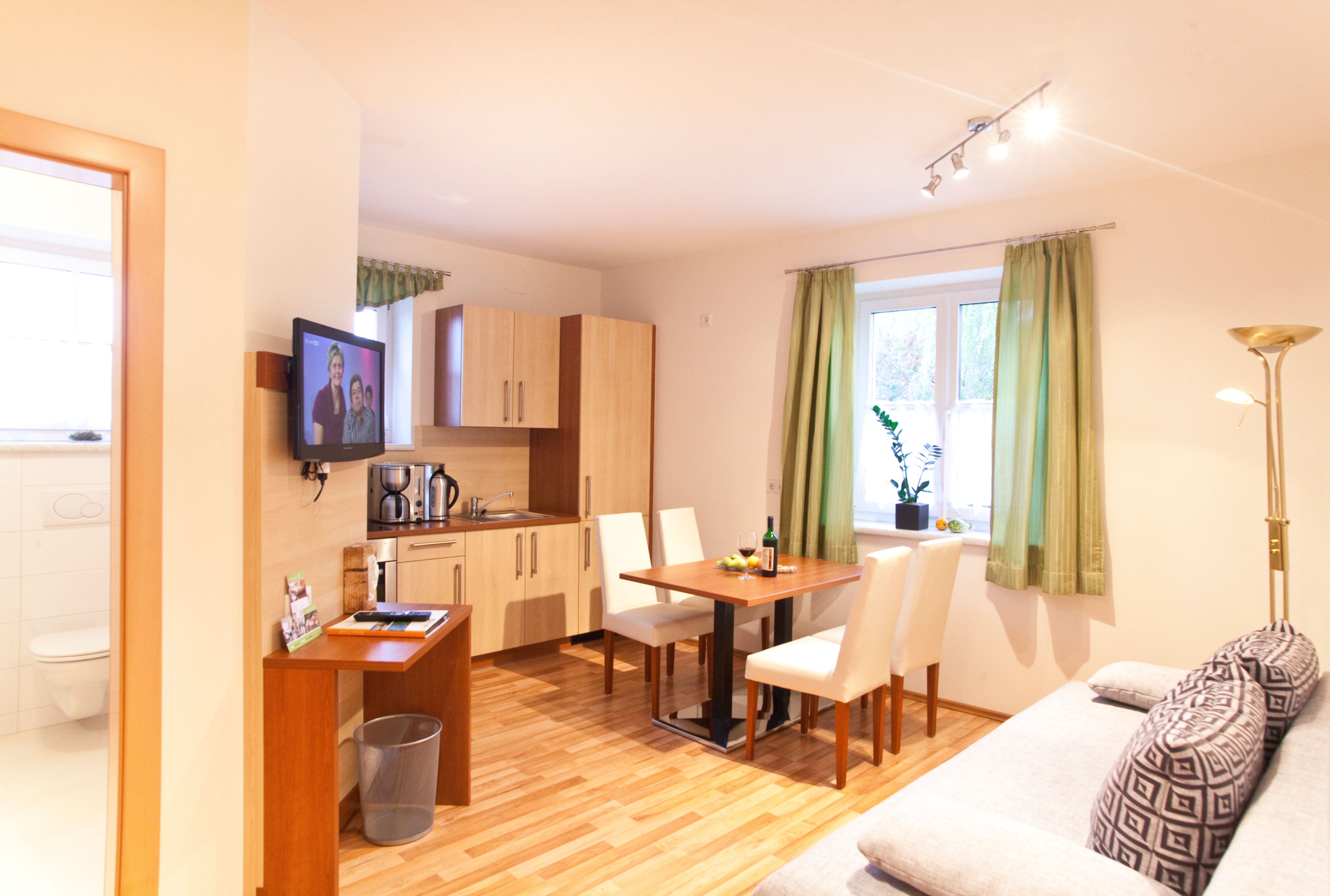 Moderní kuchyně s jídelním stolem, pohovkou a TV ve světlém pokoji.