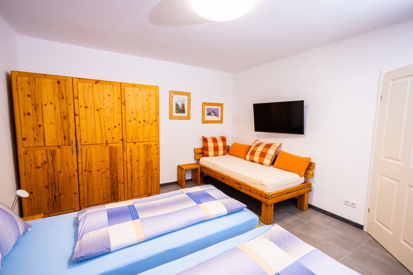 Ložnice s dřevěným nábytkem, dvěma lůžky, pohovkou, TV a obrázky na stěně.