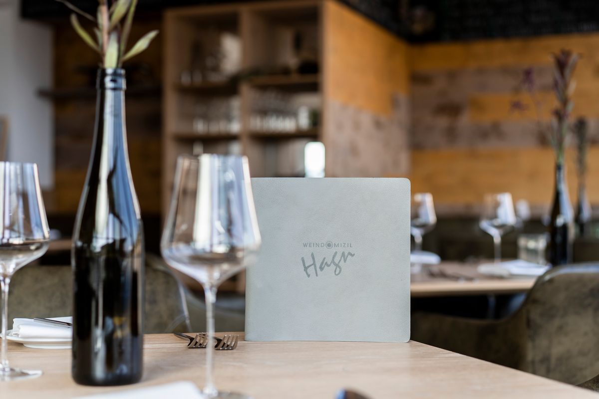 Prostřený stůl v restauraci se sklenicemi na víno, lahví vína a jídelním lístkem.