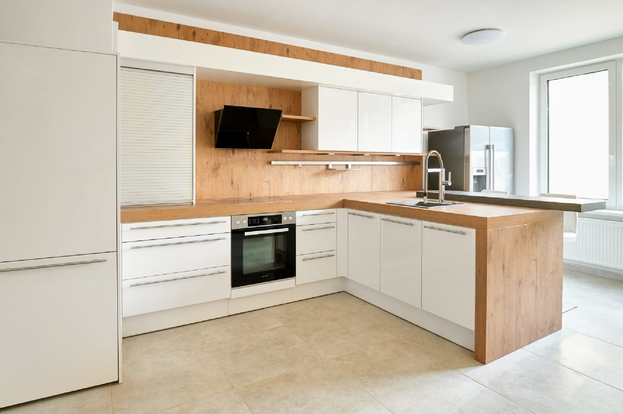 Moderní kuchyňská linka v bílých a dřevěných tónech, sporák, dřez a velké okno.