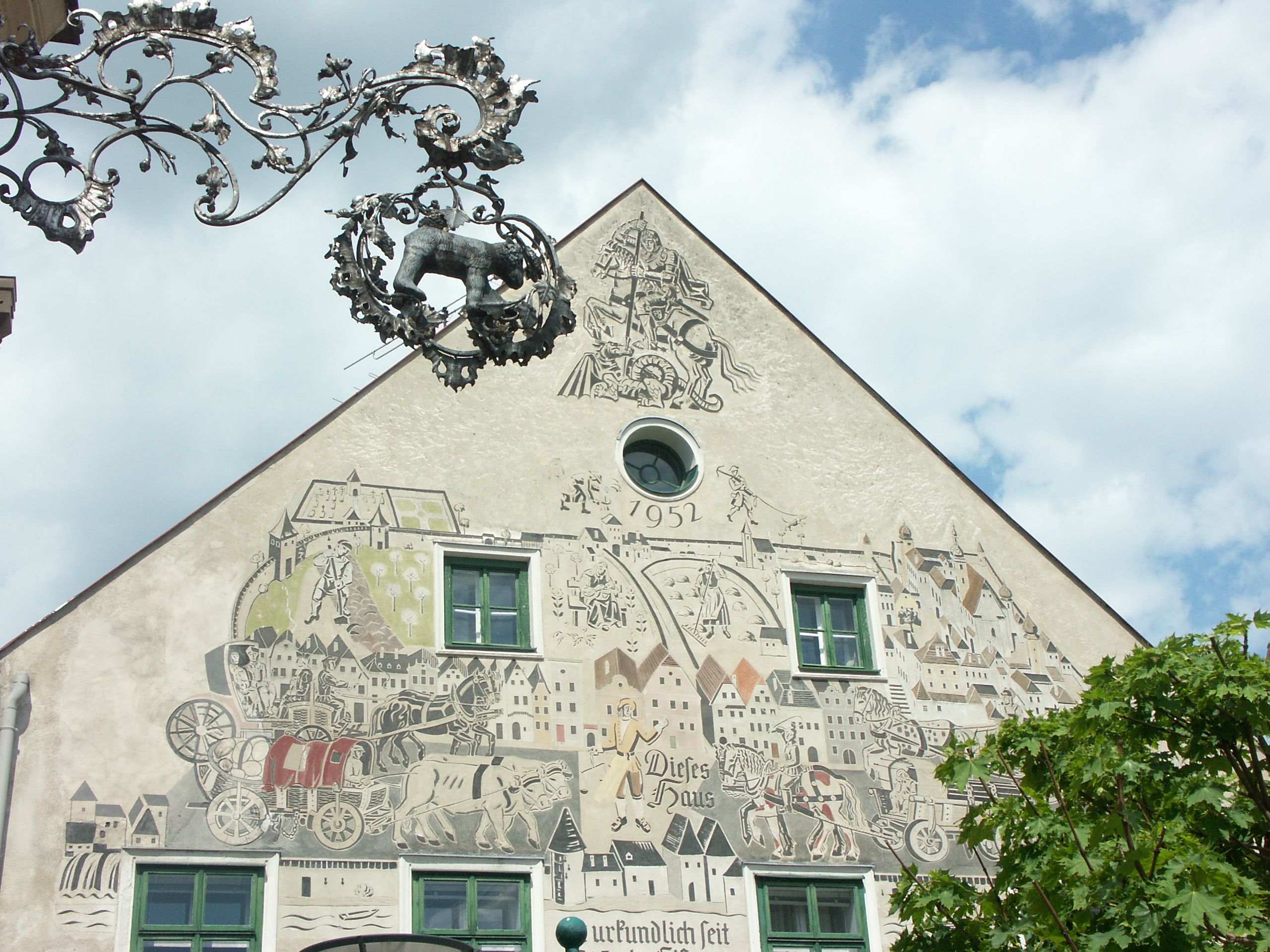 Fasáda domu s uměleckými díly ve sgrafitech a ozdobným kovovým nápisem.
