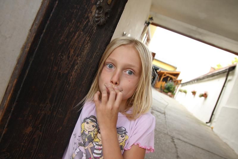 Dívka stojí v oblouku a překvapeně se dívá do kamery.