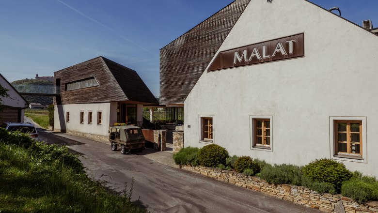 Vnější pohled na vinařství a hotel MALAT s moderní architekturou a vozidlem v popředí.