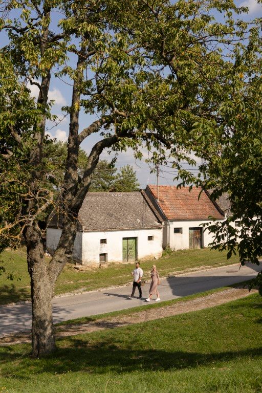 Dva lidé procházejí kolem starých budov na venkově.