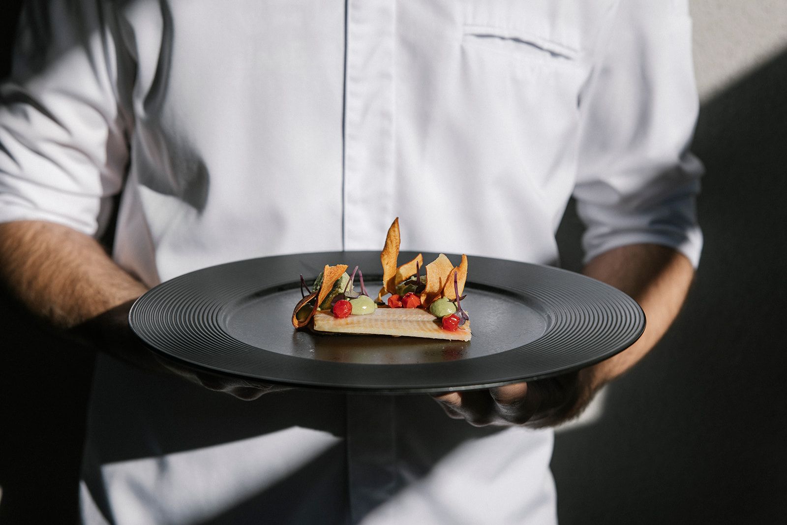 Osoba v bílé košili drží talíř s důmyslně připraveným gurmánským pokrmem.