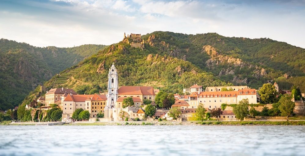 Pohled na Dürnstein se zříceninou kláštera a hradu před zalesněnými kopci.
