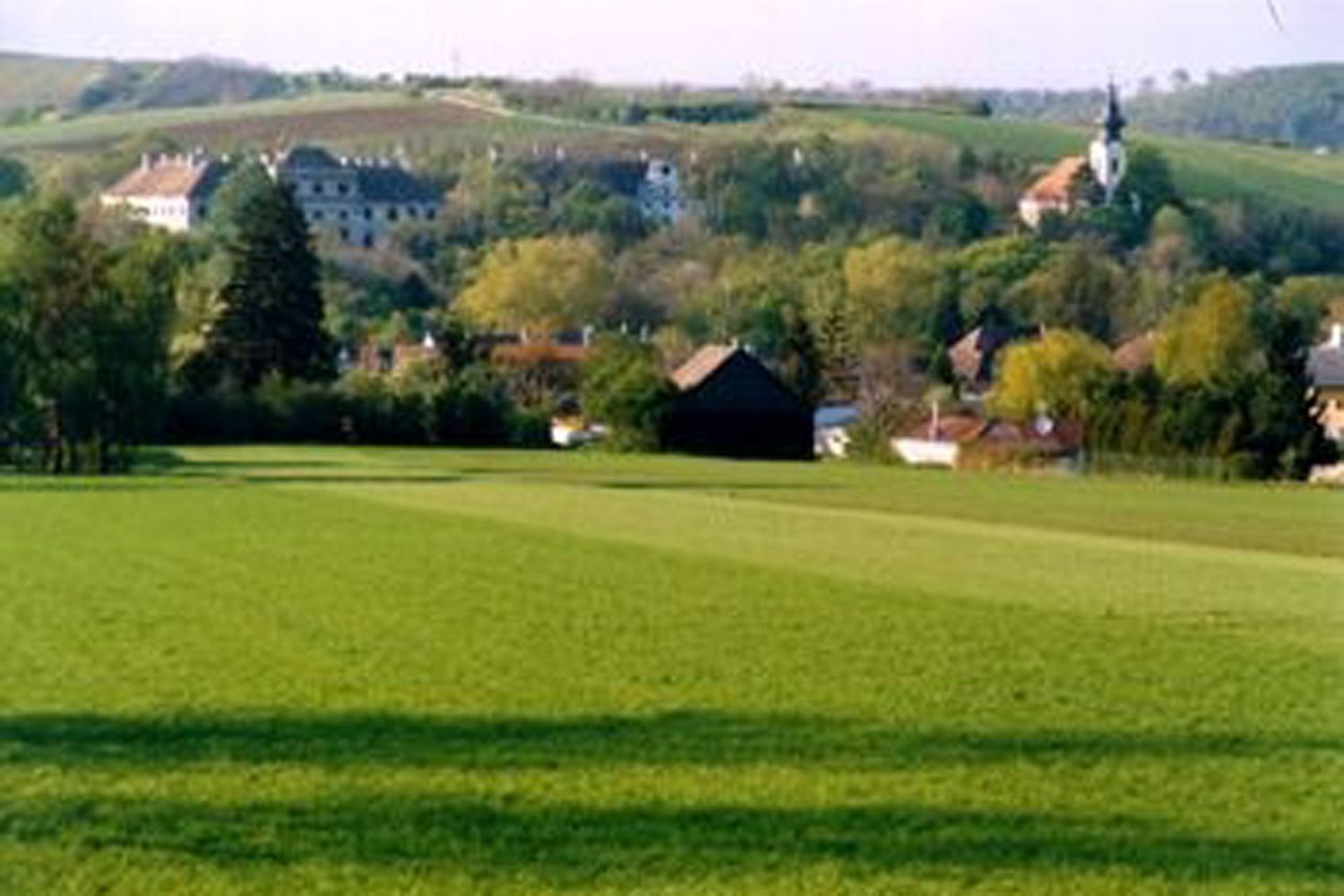 Zelené louky s vesnicí a kostelem v pozadí.