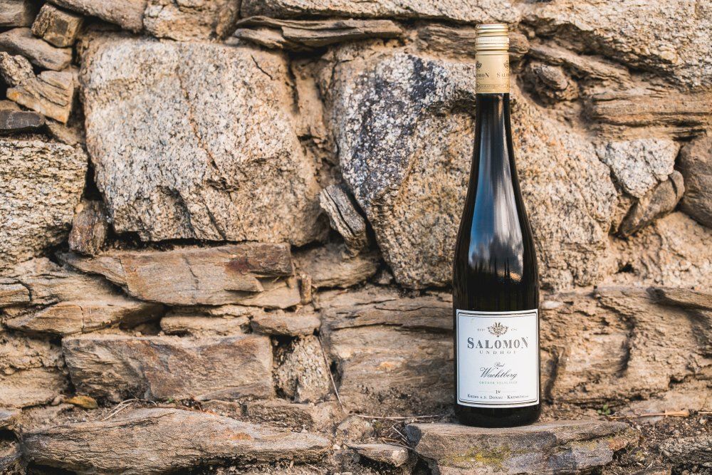 Láhev vína před kamennou zdí.