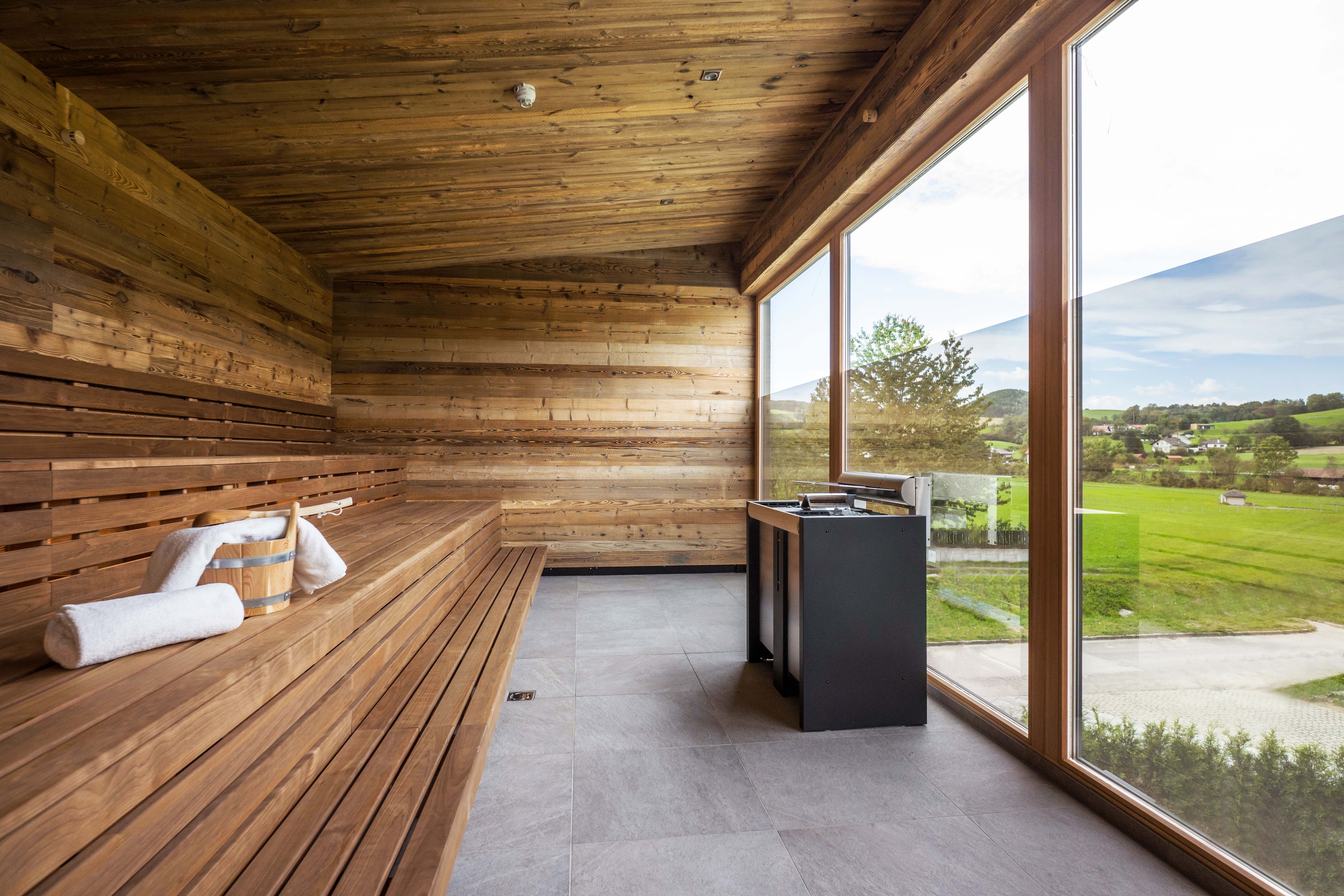 Moderní sauna s dřevěným obložením a velkým proskleným průčelím s výhledem do zeleně.