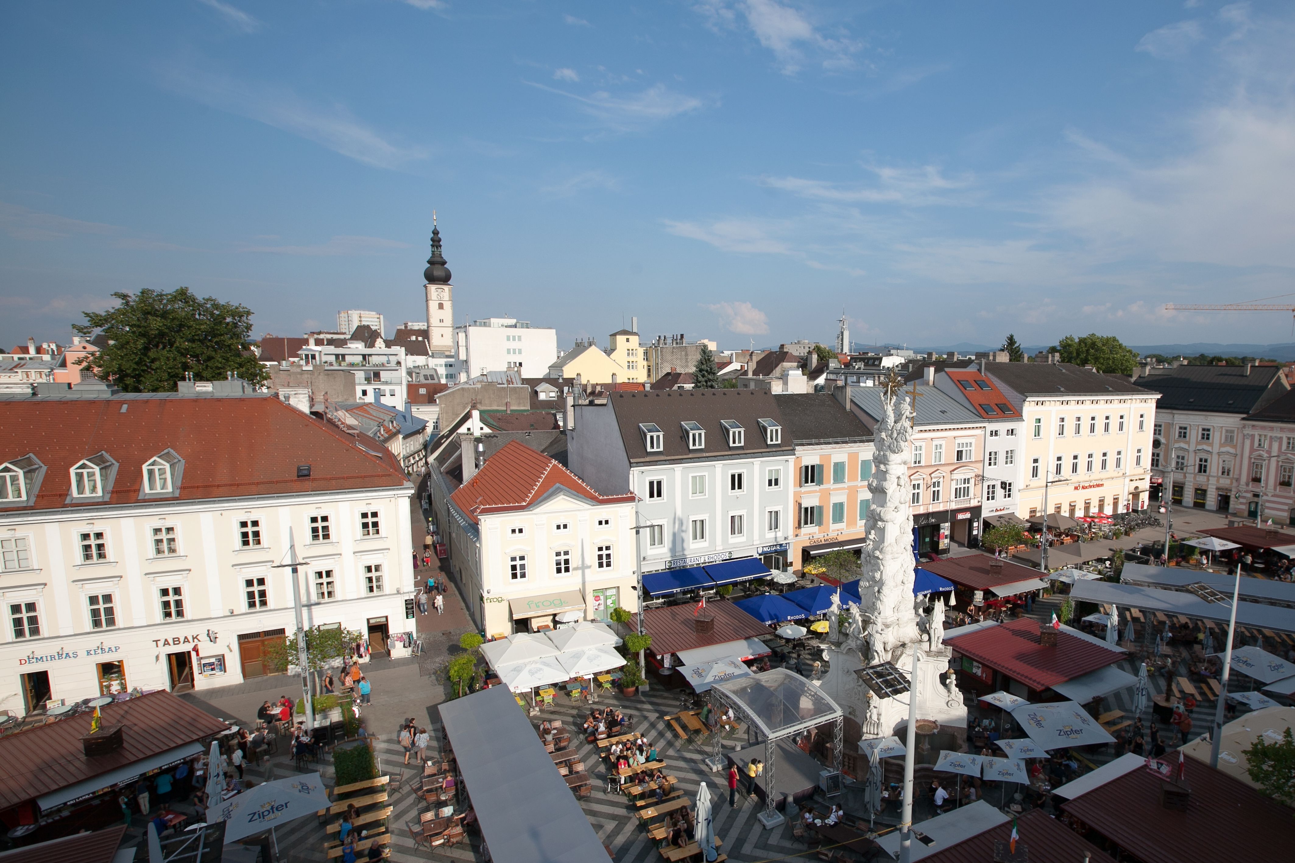 Letecký pohled na rušné náměstí v St. Pöltenu se stánky a věží v pozadí.