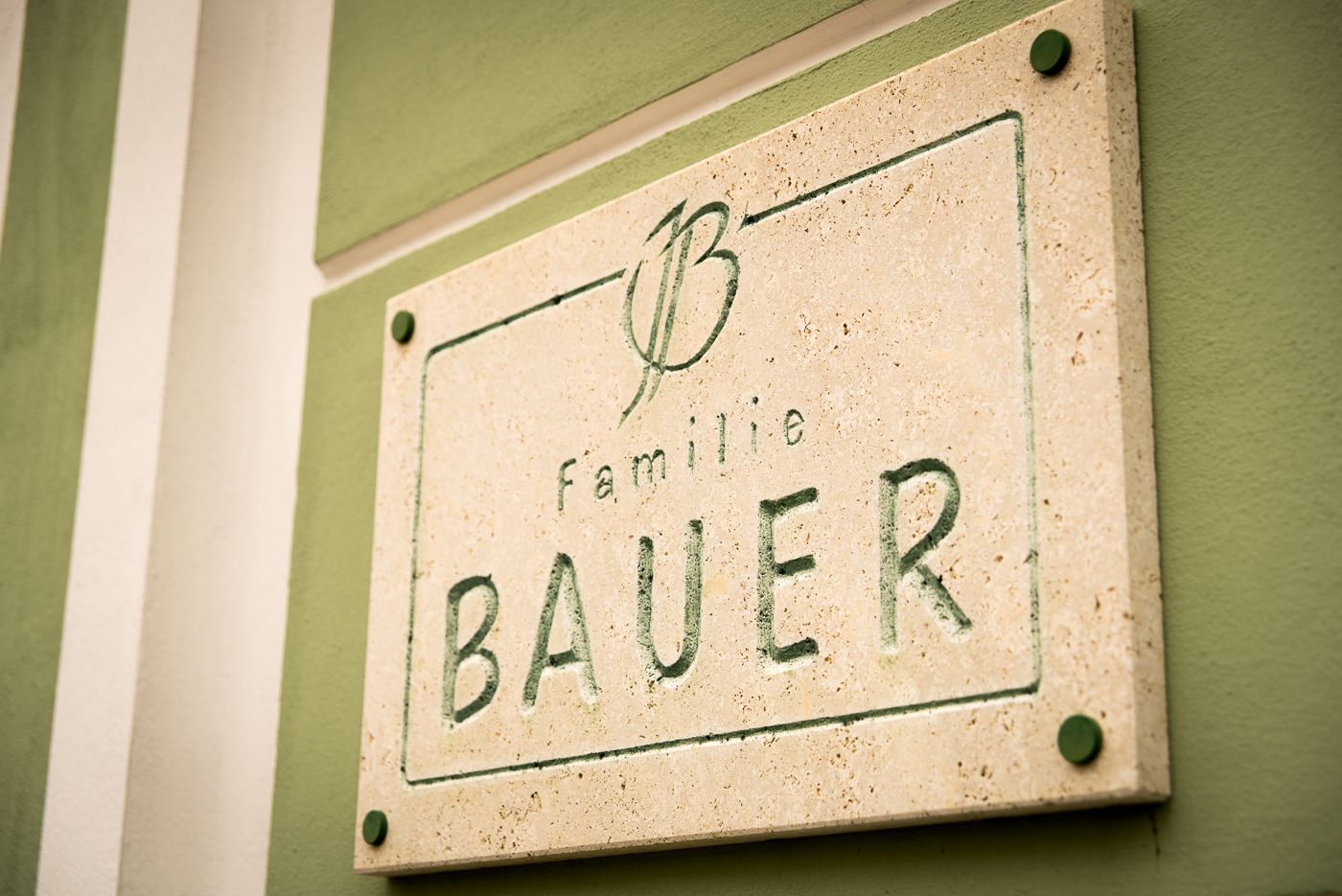 Kamenná deska s nápisem "Familie Bauer" na zelené zdi.
