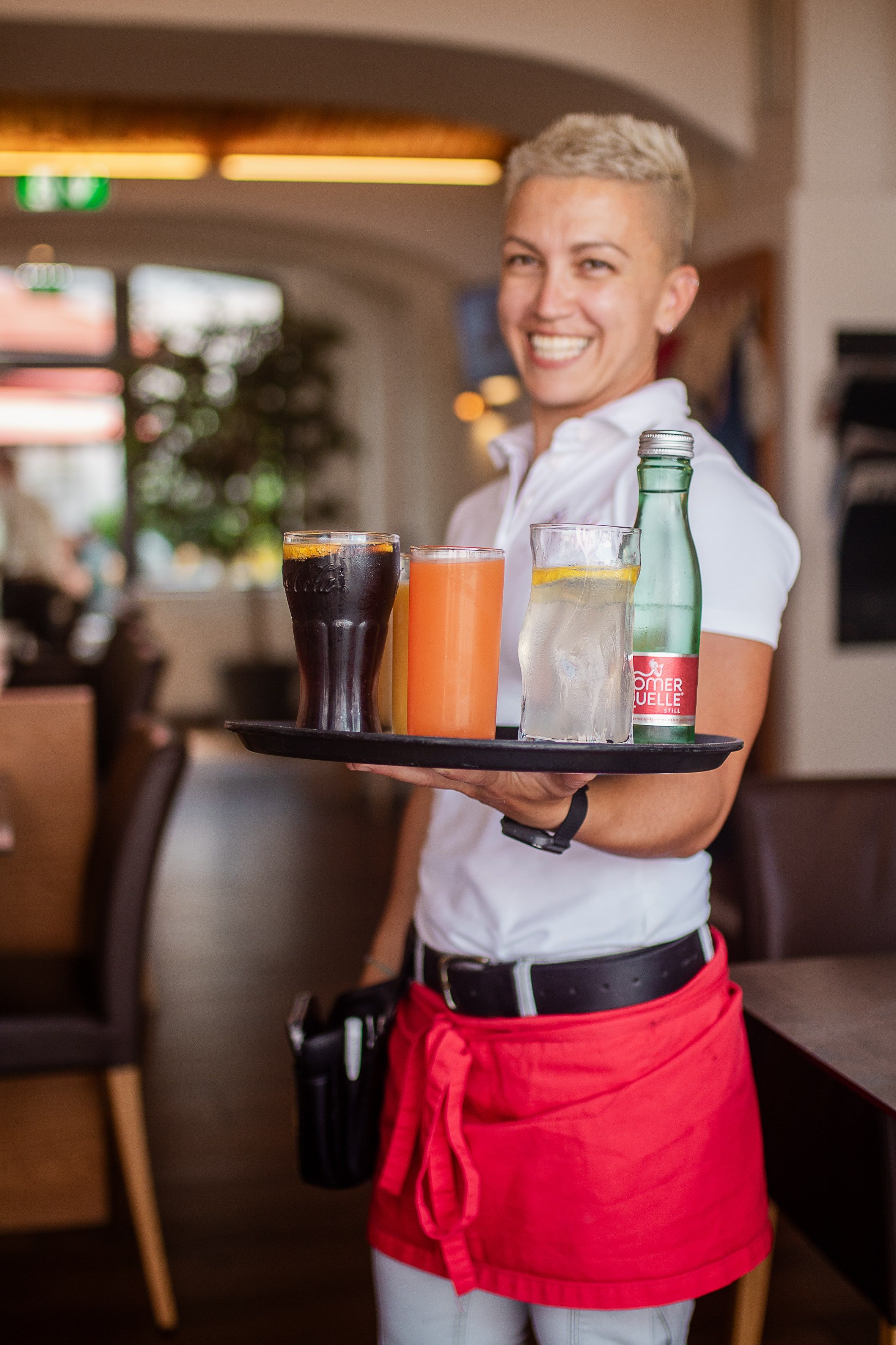 Usměvavá servírka v restauraci nese tác s různými nápoji.