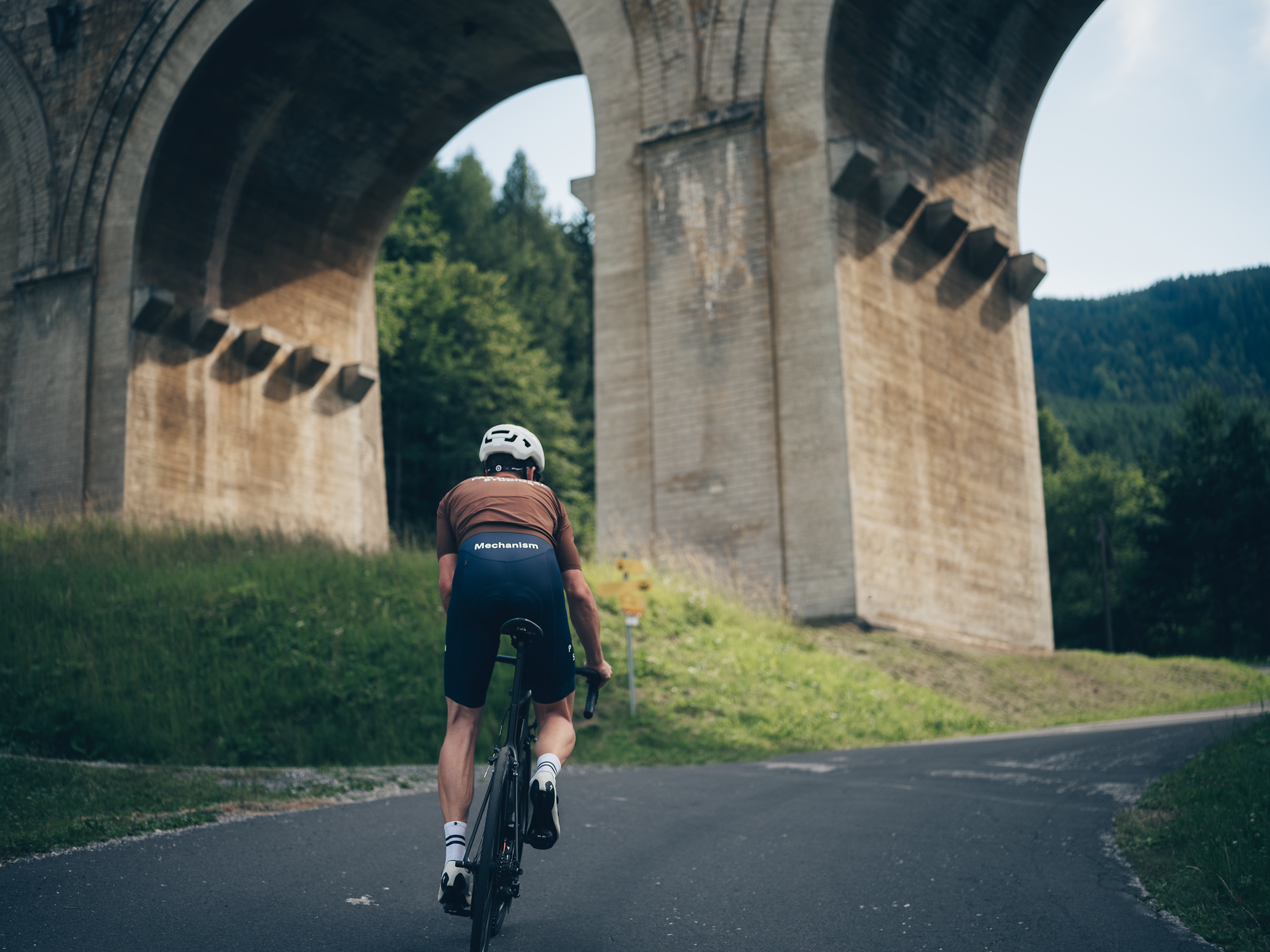 Ein Radfahrer gleitet mit Leichtigkeit auf einer kurvenreichen Straße, umgeben von majestätischen Brücken und üppigem Grün. Die frische Bergluft und die beeindruckende Landschaft laden dazu ein, die Schönheit der Natur in vollen Zügen zu genießen.