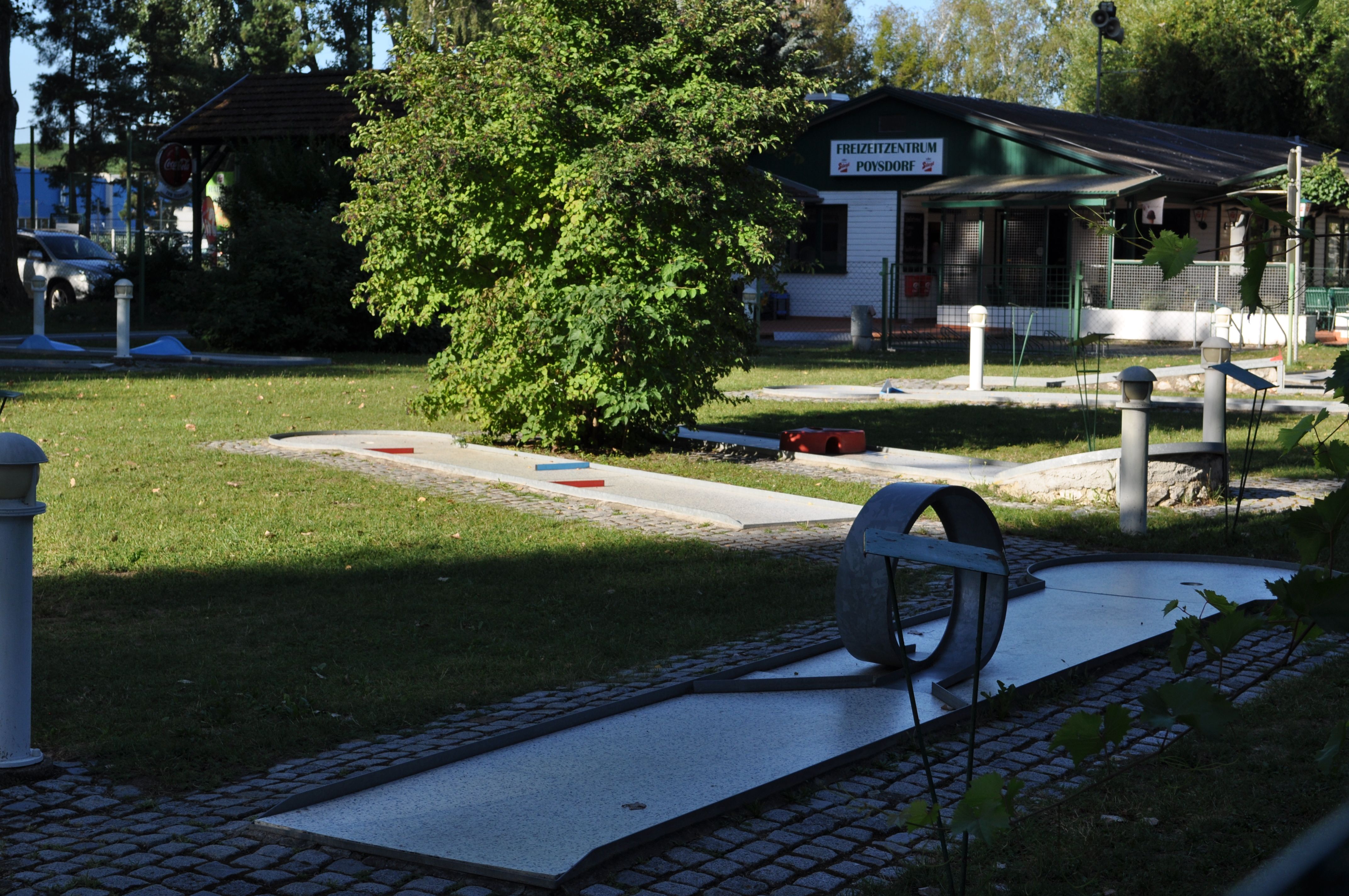 Minigolfové hřiště s překážkami a budovou v pozadí.