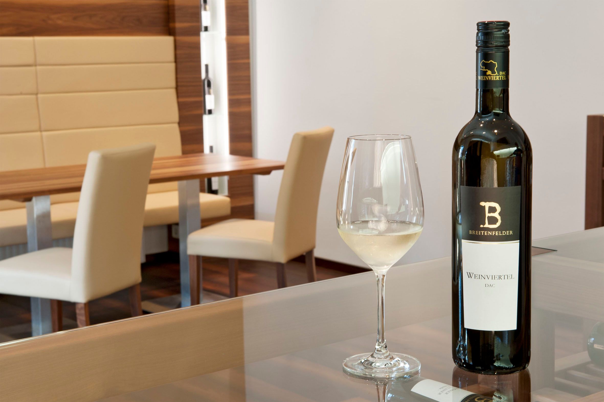 Degustační místnost s lahví bílého vína a naplněnou sklenicí na stole.