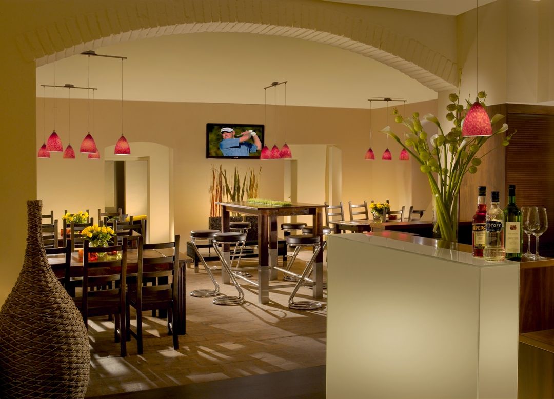 Pohled do interiéru stylové restaurace s moderním nábytkem a červenými závěsnými lampami.