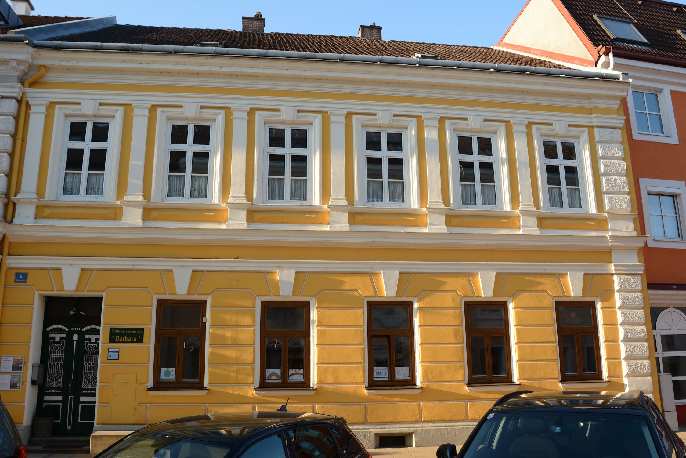 Žlutá budova s bílými okenními rámy a dekorativními prvky v Pöchlarnu.