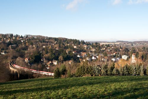 Krajina s vlakem na viaduktu v Eichgrabenu, obklopená kopci a domy.