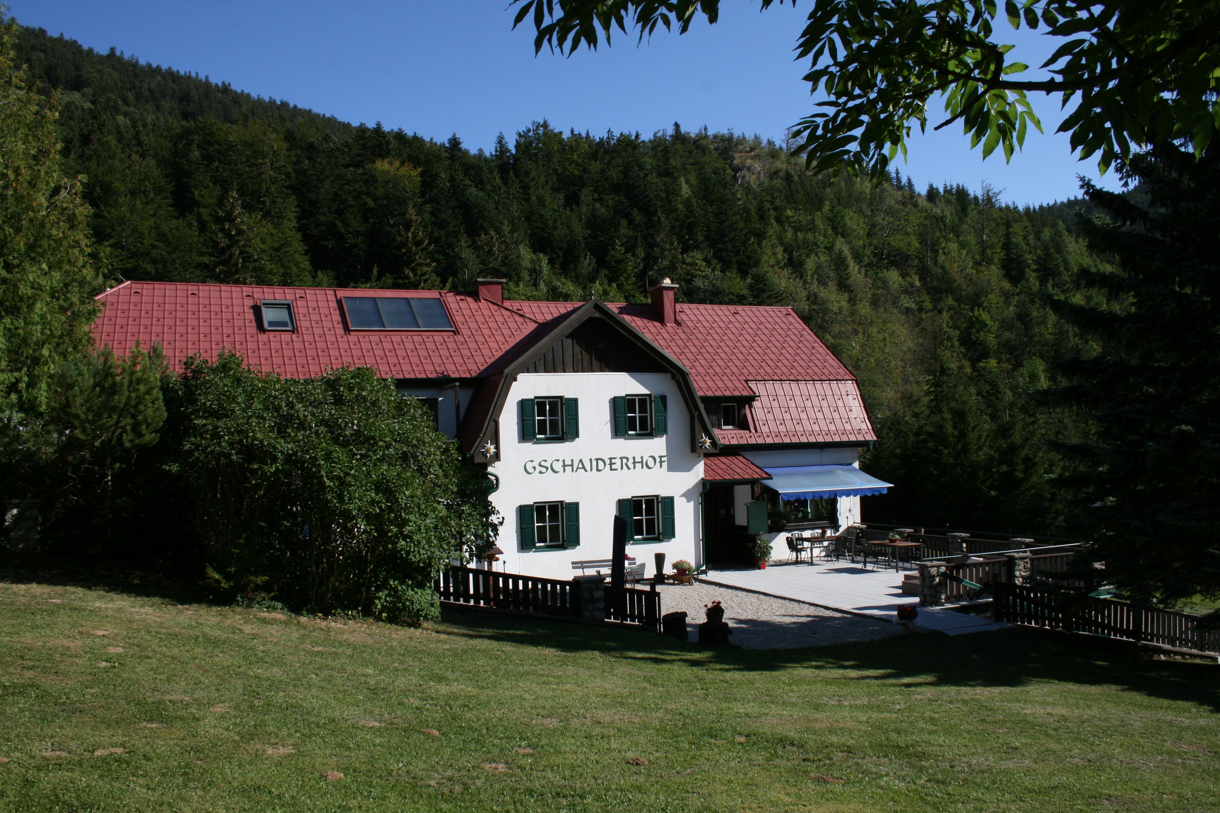 Tradiční dům s červenou střechou, obklopený lesy a loukami, s označením "Gschaiderhof".