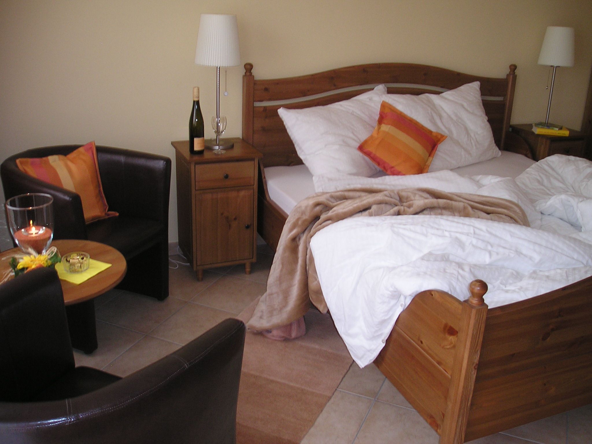 Útulný pokoj pro hosty s manželskou postelí, nočním stolkem, lampou, křeslem a stolem.