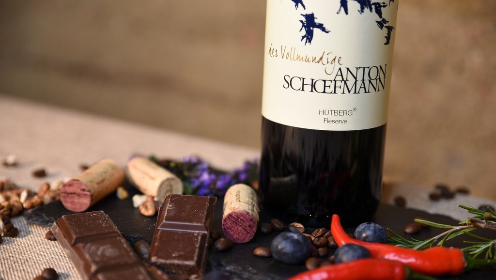 Láhev vína s čokoládou, zátkou a kořením na stole.