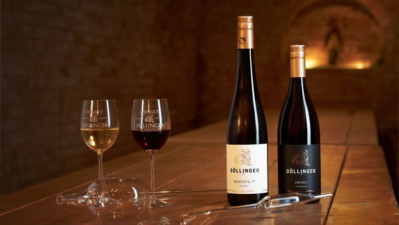 Dvě sklenice na v&iacute;no a dvě l&aacute;hve v&iacute;na na dřevěn&eacute;m stole ve vinn&eacute;m skl&iacute;pku.