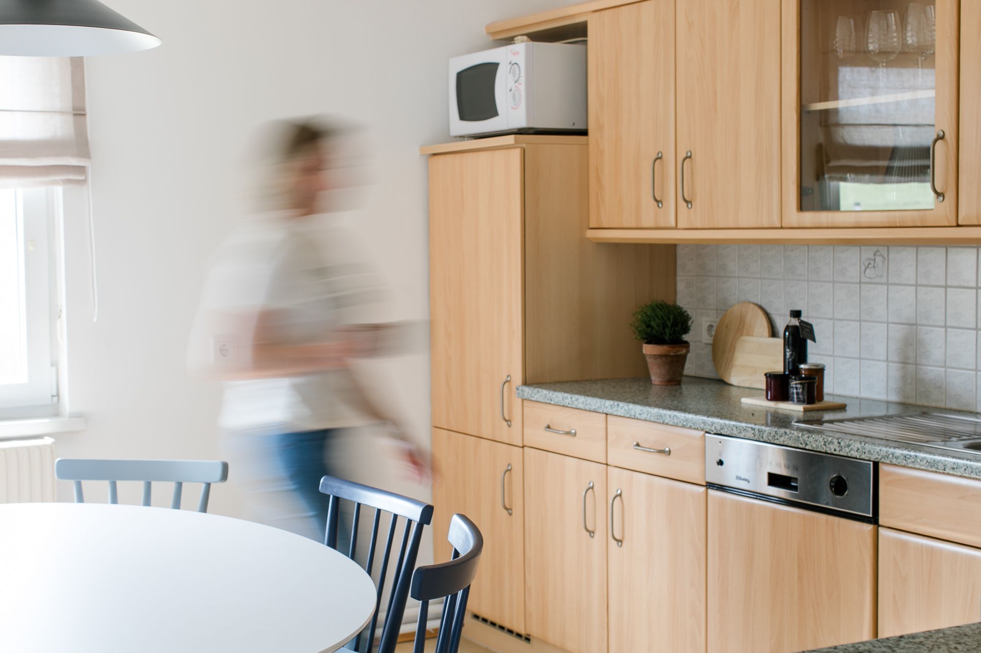 Moderní kuchyně s dřevěným nábytkem a jednou osobou v pohybu.