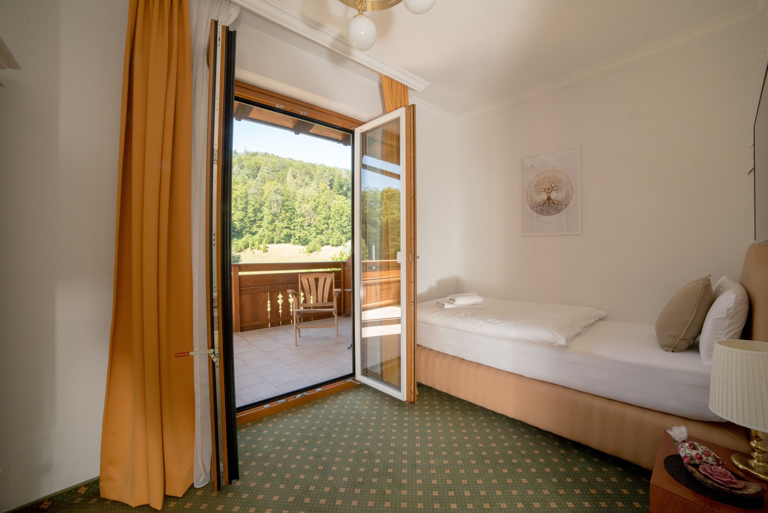 Jednolůžkový pokoj s balkonem, samostatná postel, otevřené balkonové dveře, výhled do zeleně.