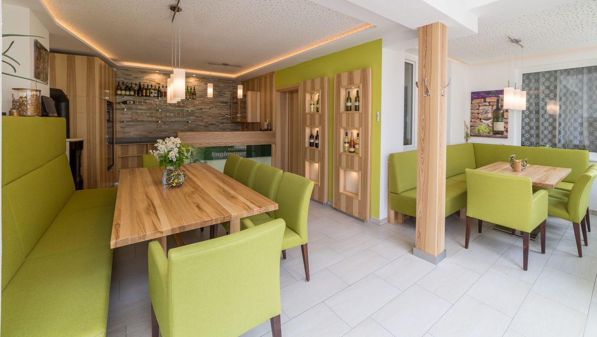 Moderní degustační místnost s dřevěnými stoly a zeleným čalouněným nábytkem.