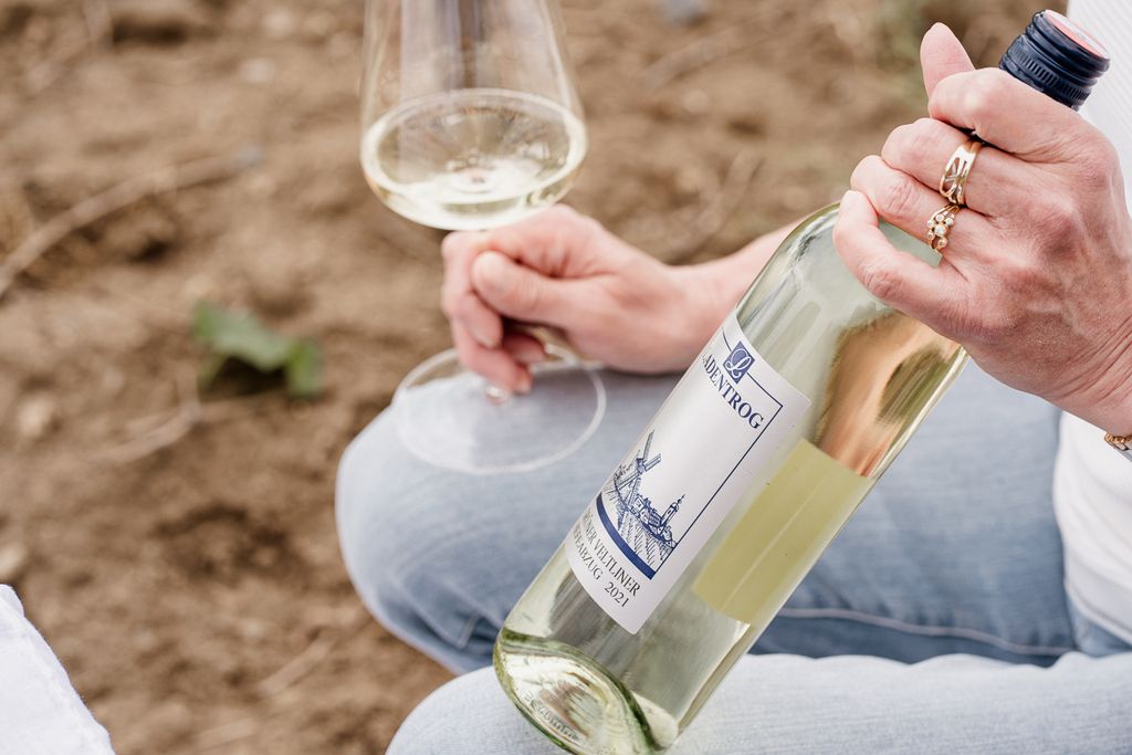 Osoba držící láhev vína a sklenici bílého vína.