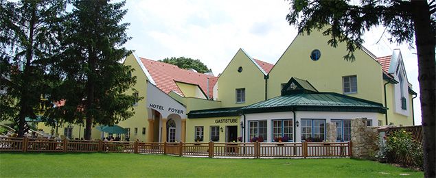 Žlutá budova s hotelem a restaurací, obklopená stromy a trávníkem.