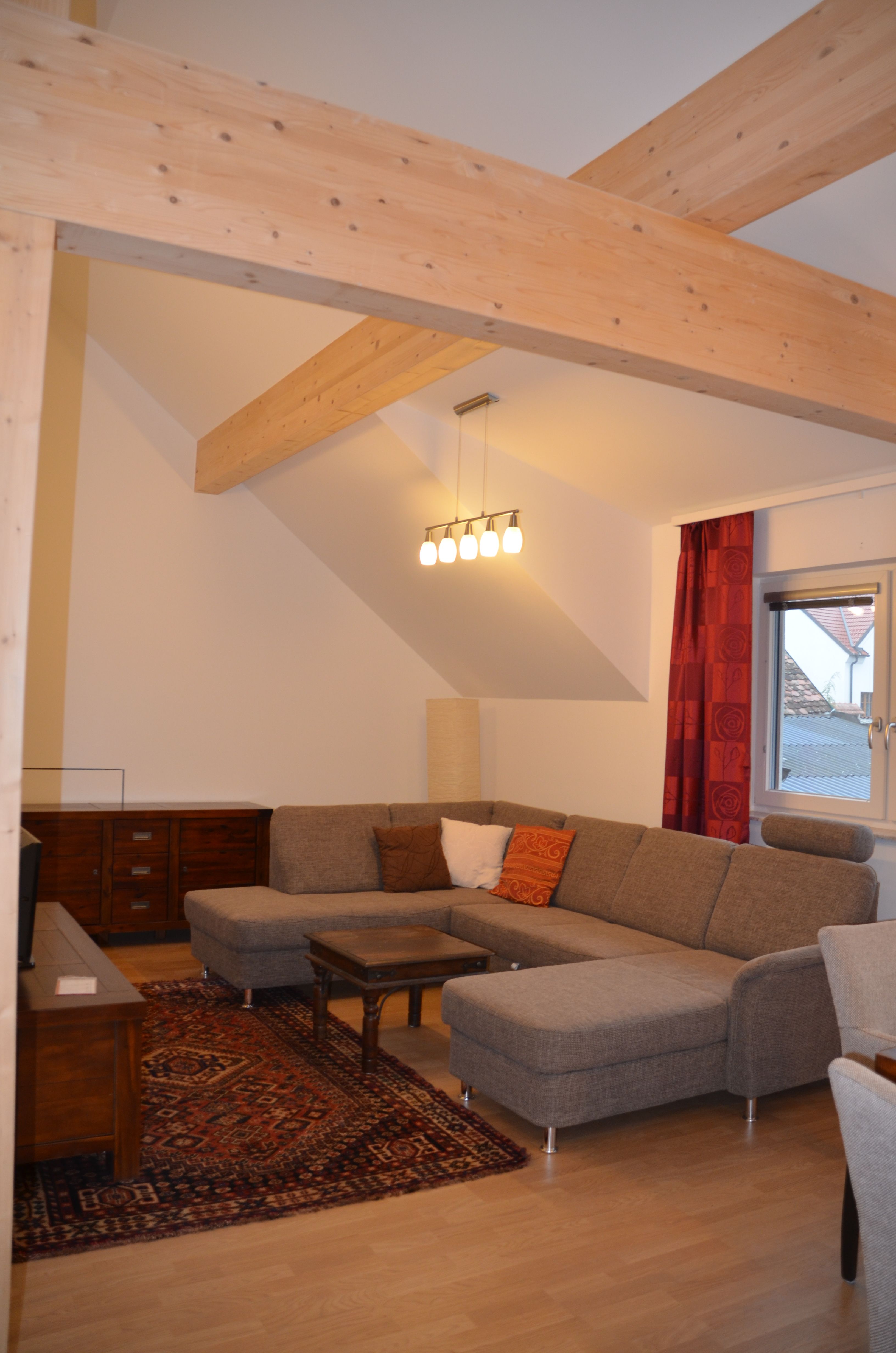 Moderní obývací pokoj s šedou rohovou pohovkou, dřevěnými trámy, kobercem a lampou.