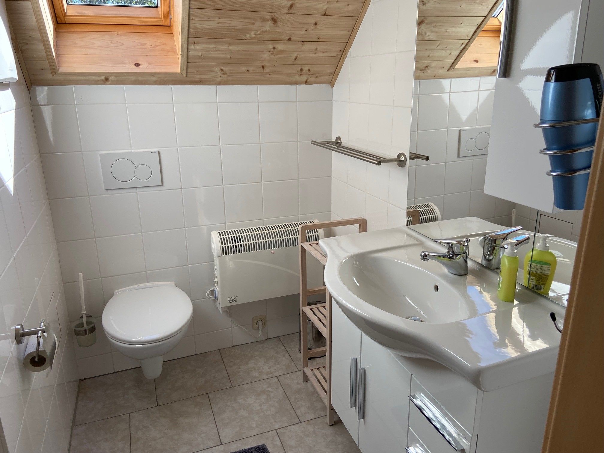 Moderní koupelna se střešním oknem, umyvadlem, toaletou a věšákem na ručníky.