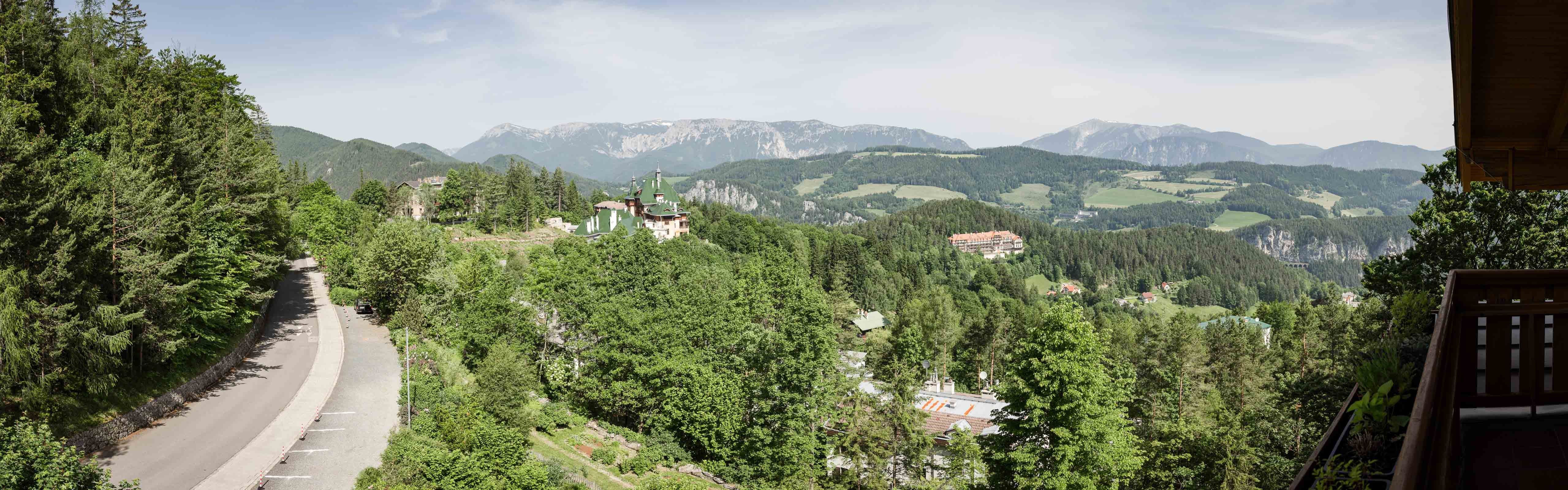 Panoramatický pohled na hornatou krajinu s lesem, silnicí a budovami.