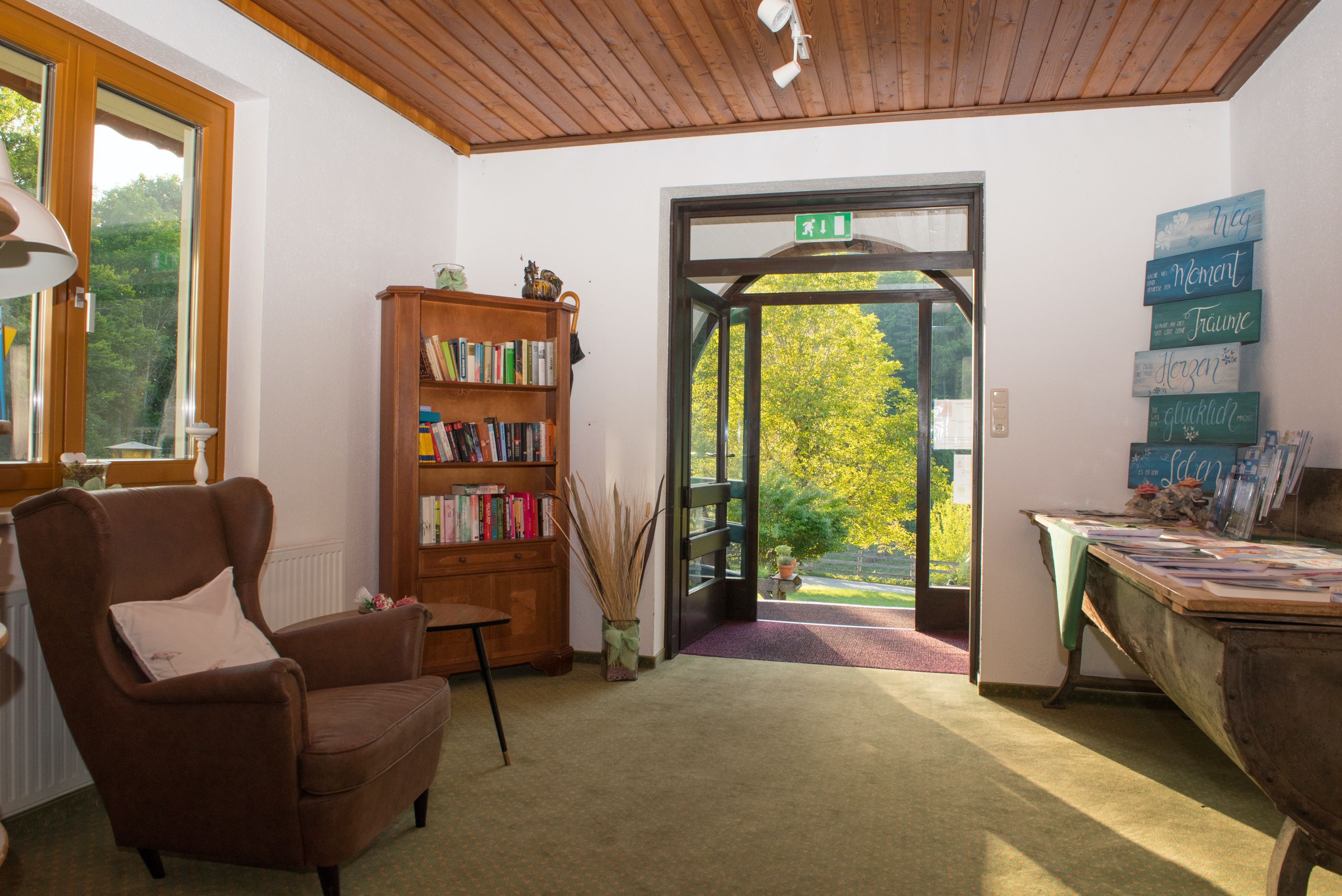Vstupní prostor s křeslem, knihovnou a otevřenými dveřmi s výhledem do zeleně.