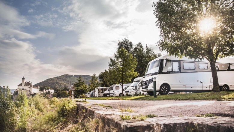 Obytn&eacute; vozy v kempu s hradem v pozad&iacute;.