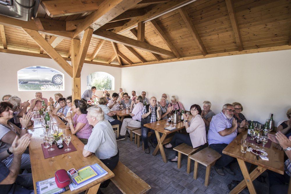 Lidé sedí u dřevěných stolů ve vinárně a klevetí.