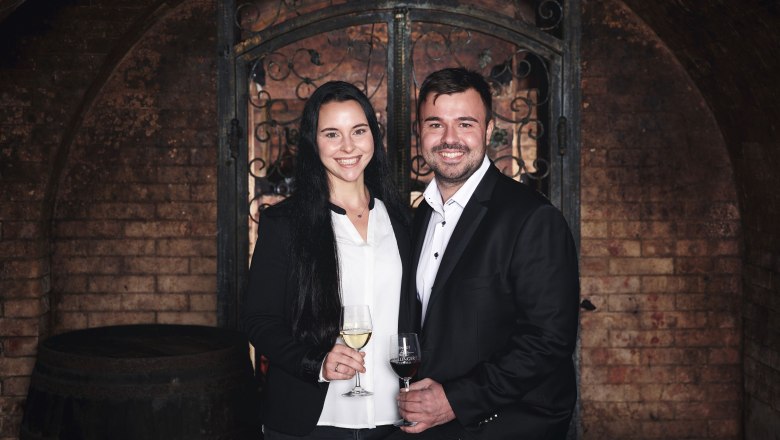 Muž a žena v elegantn&iacute;ch &scaron;atech drž&iacute; ve vinn&eacute;m skl&iacute;pku sklenice s v&iacute;nem.