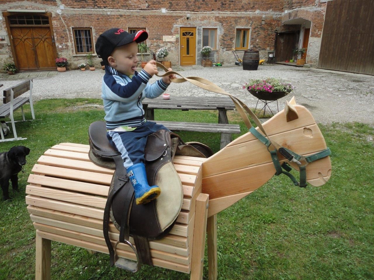 Dítě sedí venku na dřevěném koníkovi.