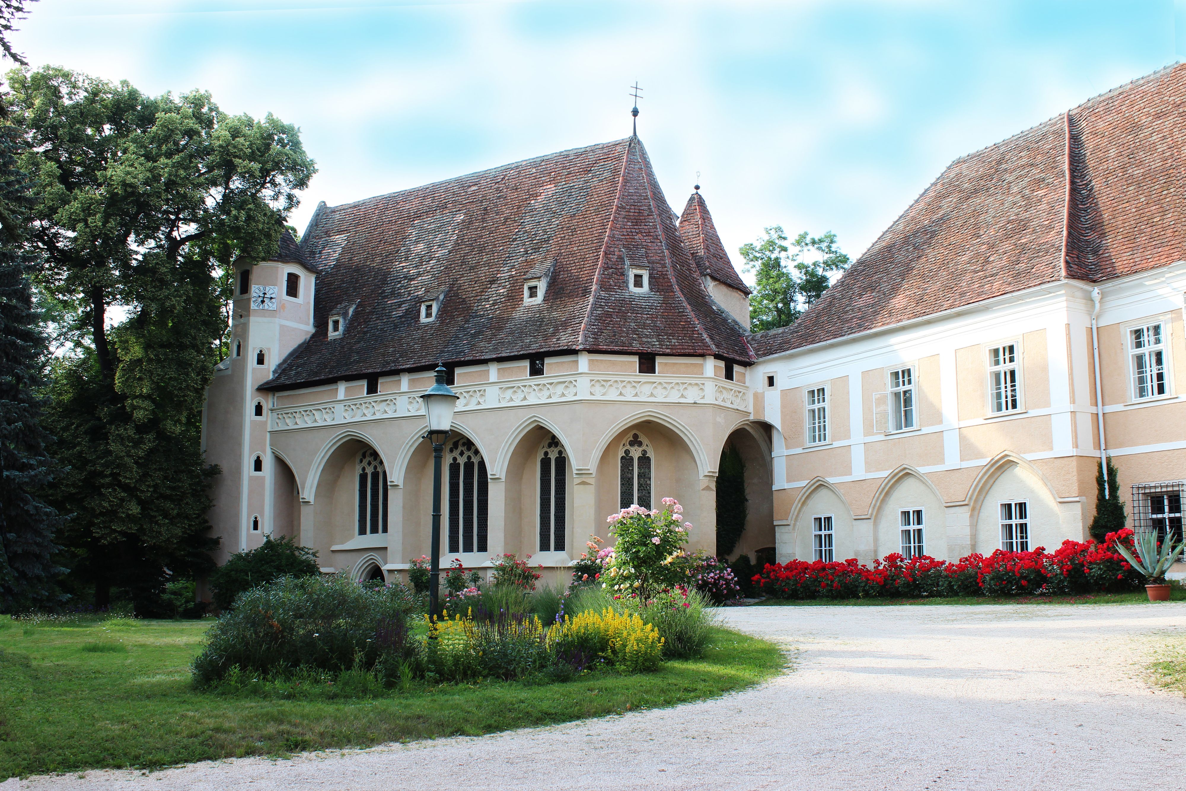 Historická budova se špičatou střechou a zahradou v popředí.