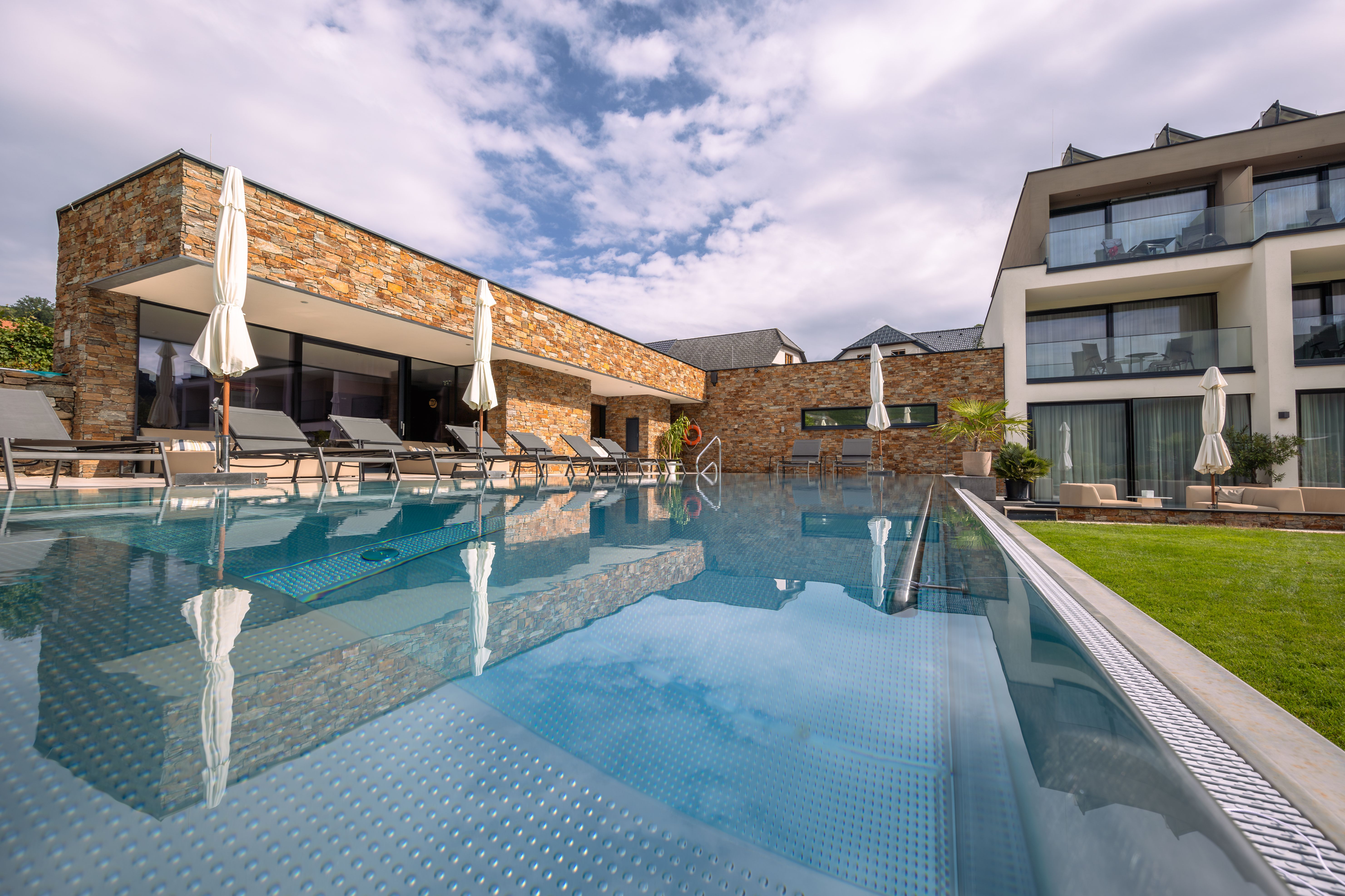 Pohled zvenčí na moderní hotel s bazénem a lehátky.