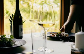 Prostřený stůl s lahví vína, sklenicemi a talířem s jídlem v restauraci.