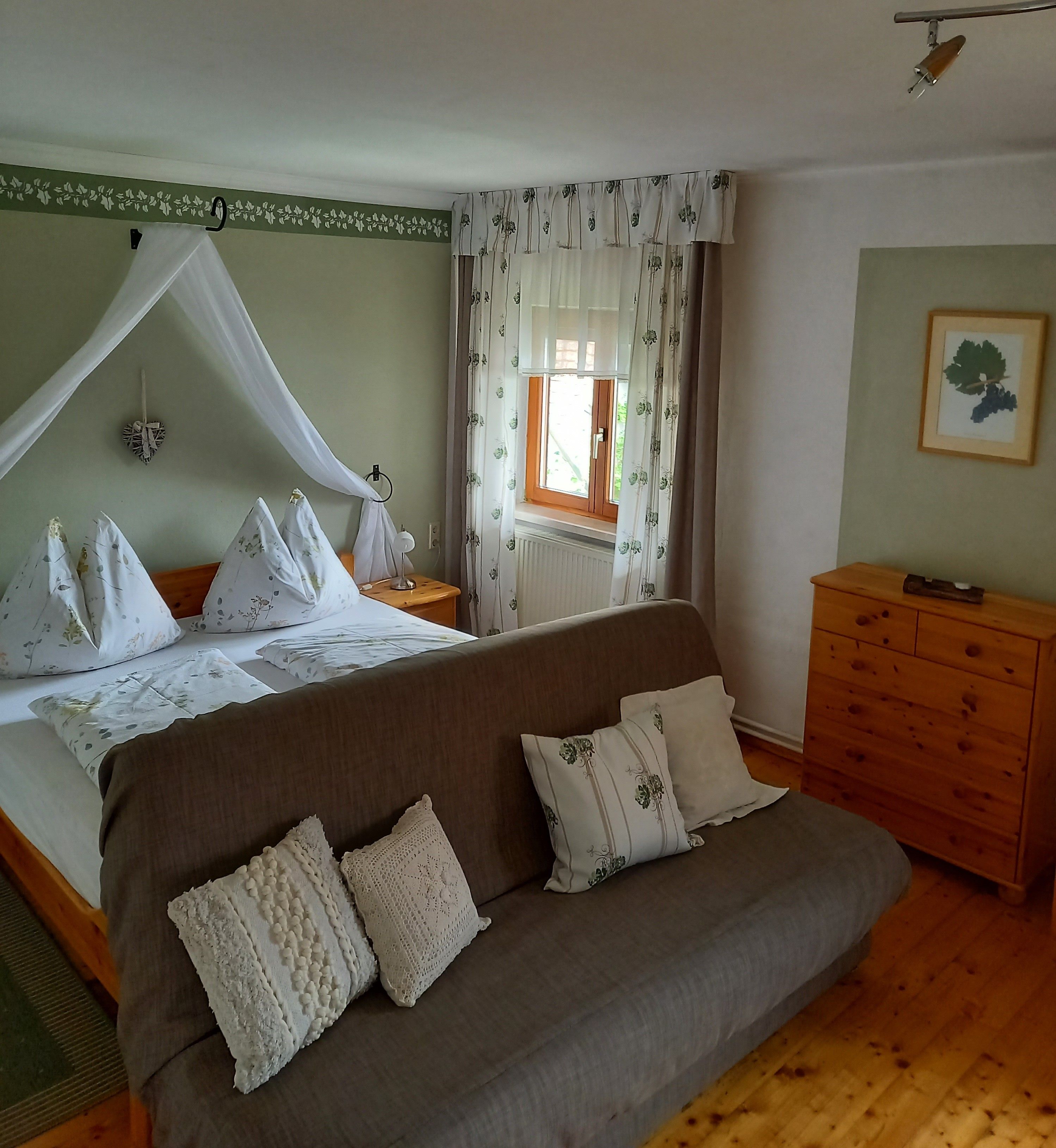 Útulný pokoj pro hosty s manželskou postelí, pohovkou a dřevěným nábytkem.