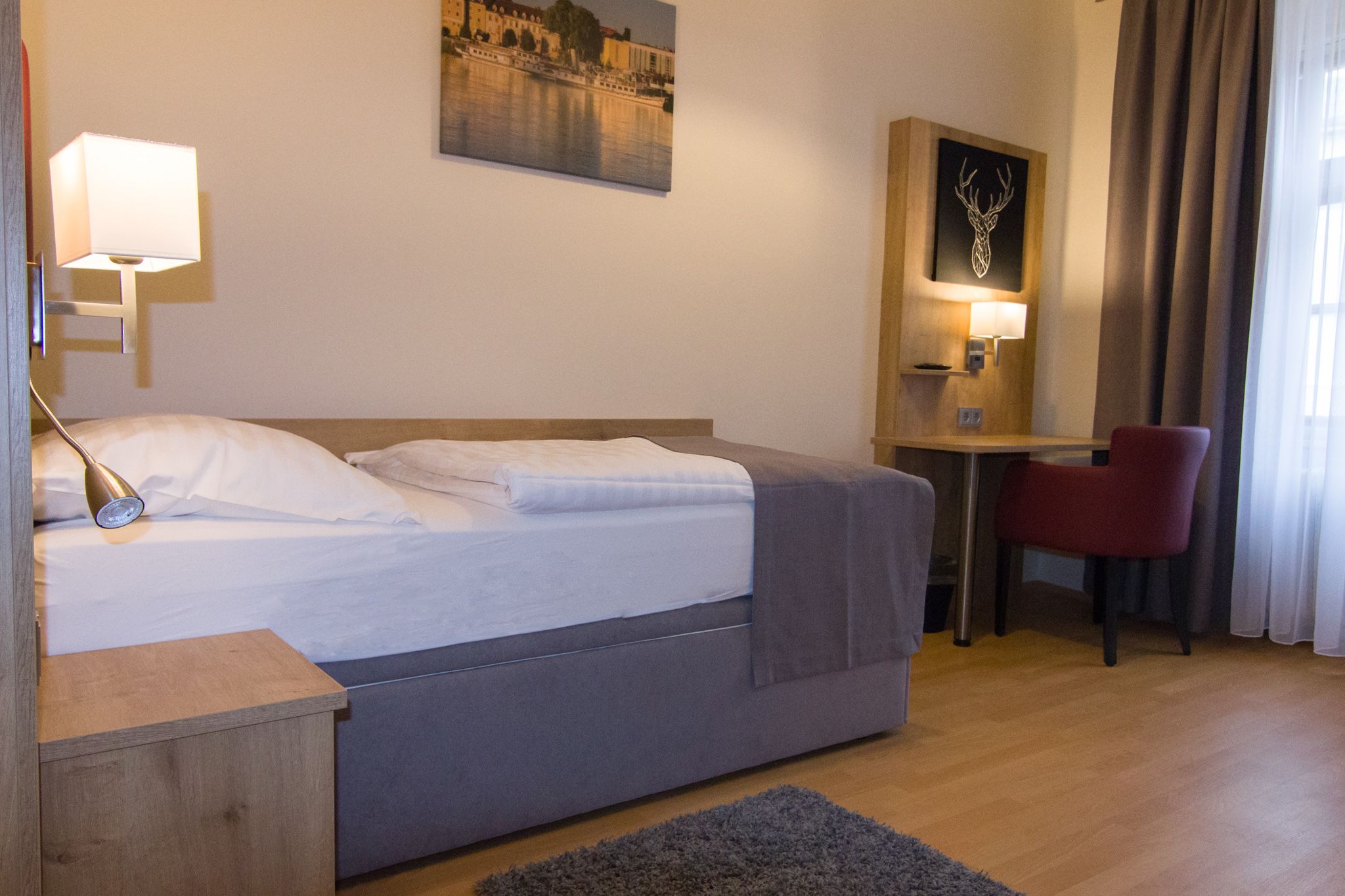 Jednolůžkový pokoj s postelí, psacím stolem a červenou židlí.